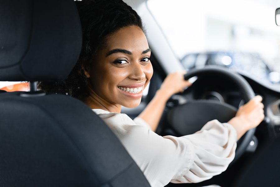 a beautiful young woman is smiling in the driver's seat of her new car.