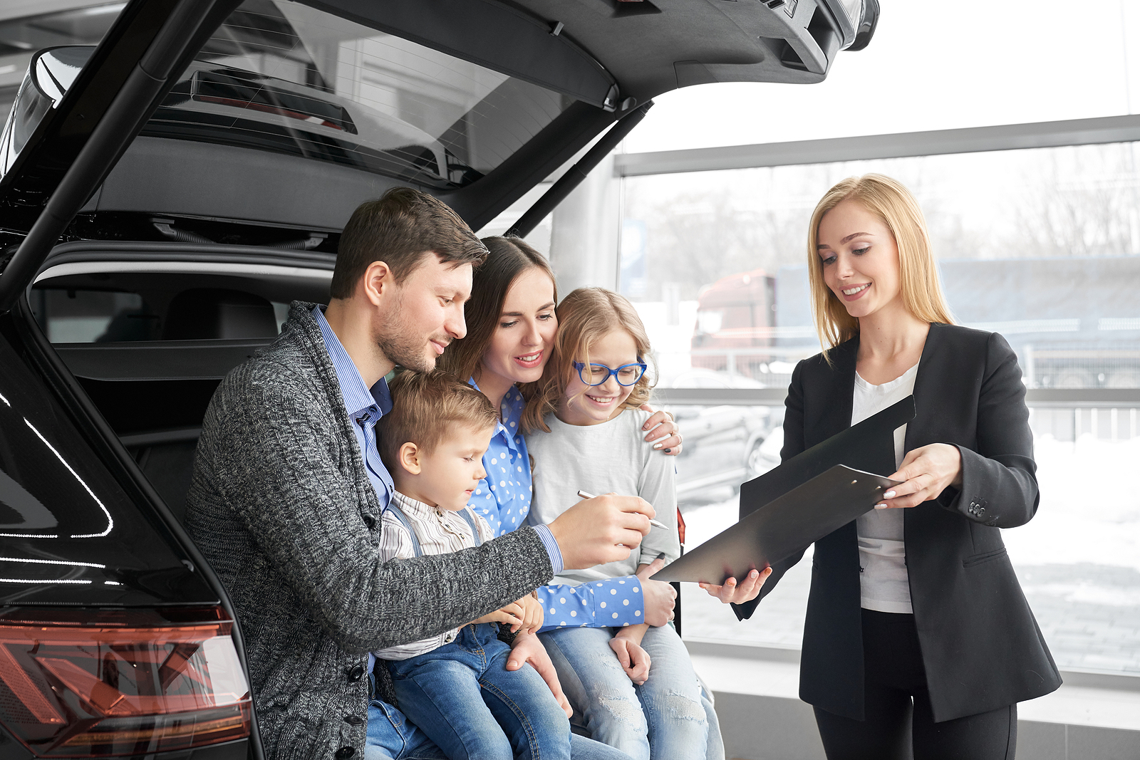 a happy family sits in the back of a new SUV as they consider buying it.