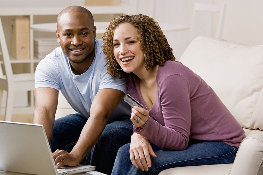 a man and woman smile as they shop with a credit card online.