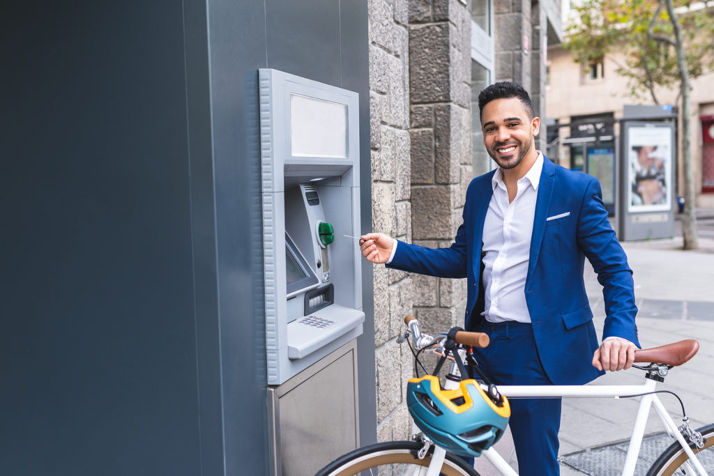 a man with a bicycle takes money out of an ATM
