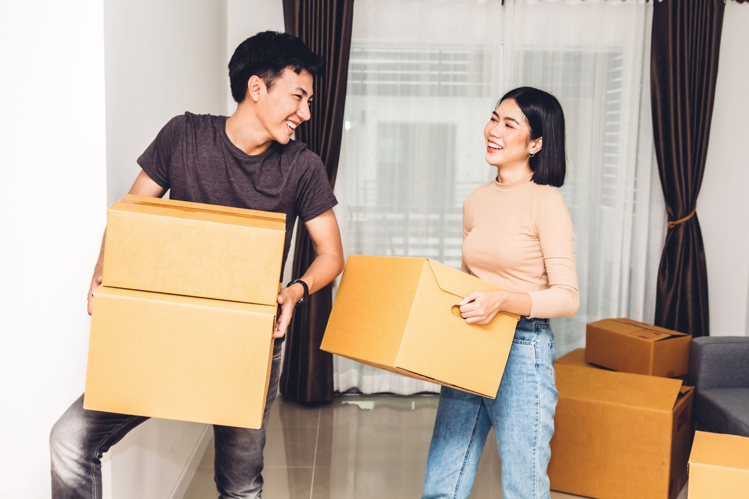 A happy young couple carry boxes into their new home after learning how to be a competitive home buyer in the Cleveland/Athens market.