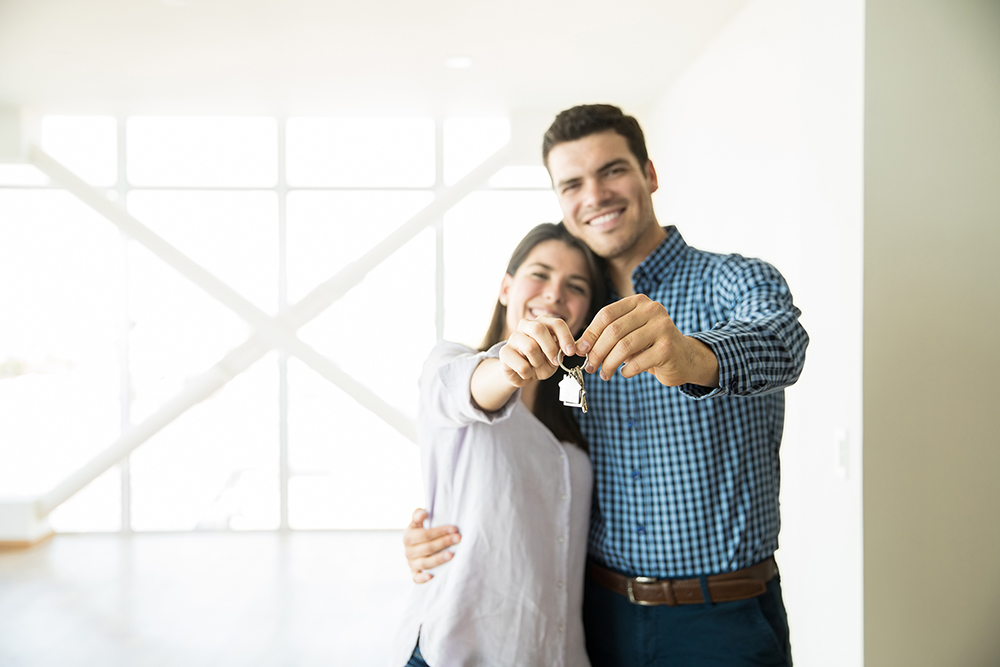 A happy couple shows off keys to their new home after comparing credit union vs. bank mortgage.