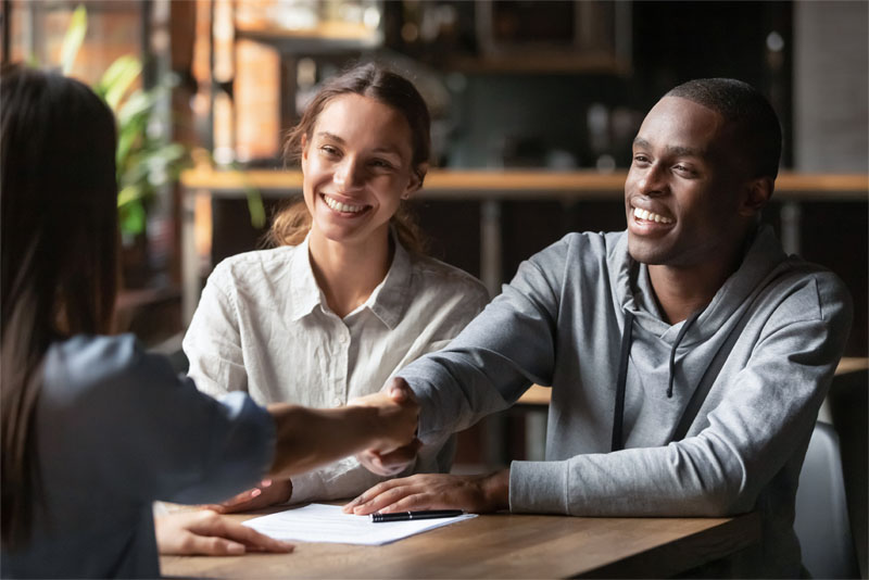 A young couple shaking hands with a lender after a mortgage refinance.