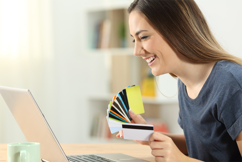 A woman holding several up different credit cards to choose from as she shops online.