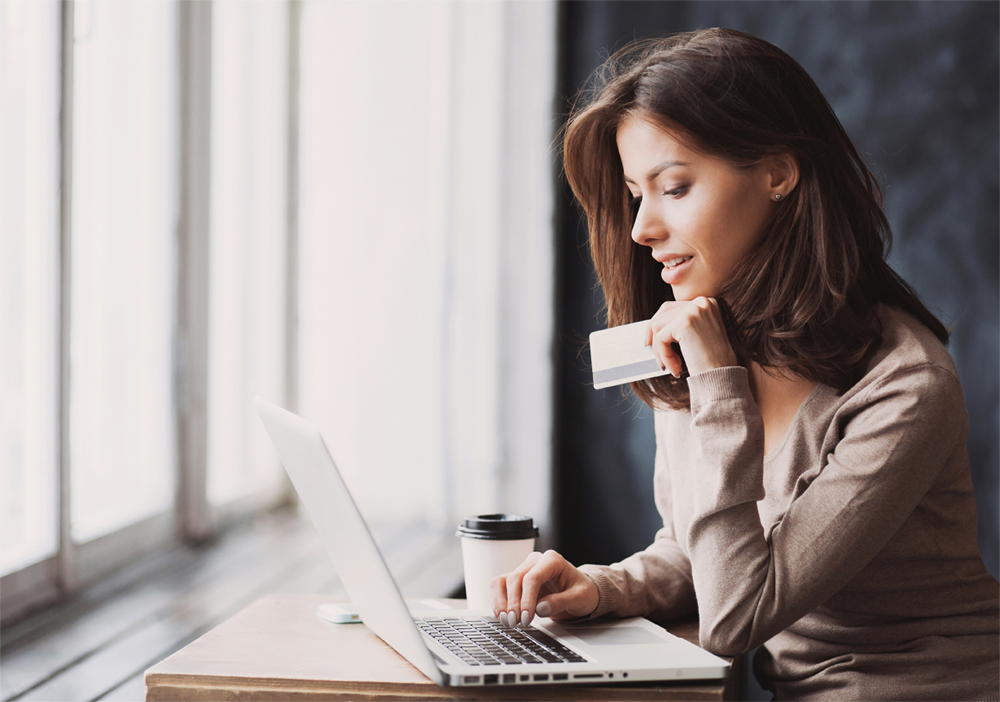 A woman holds her credit card while researching credit card apr on her laptop.