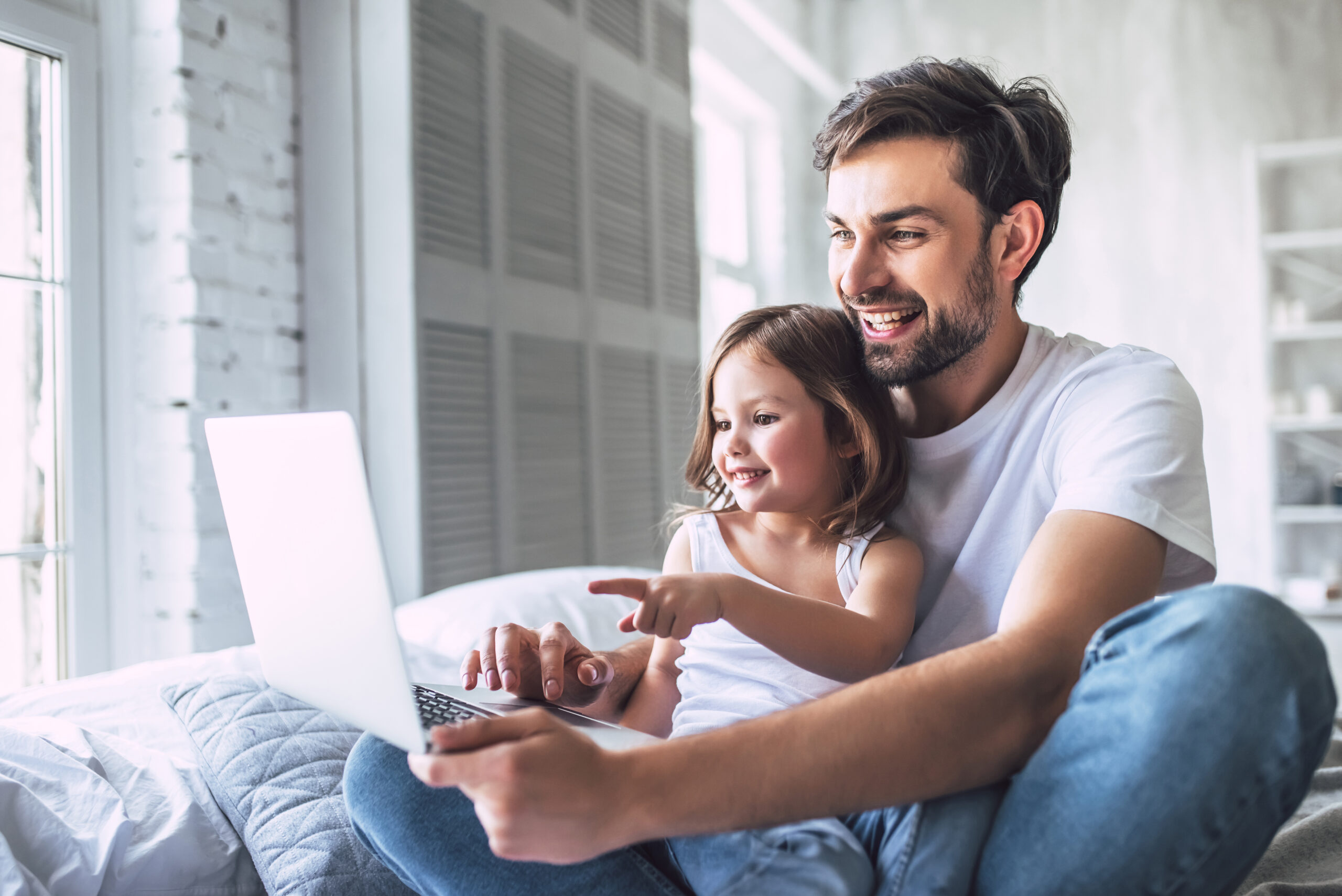 Dad with young daughter at home with laptop together as he applies for a Bowater CU account online.
