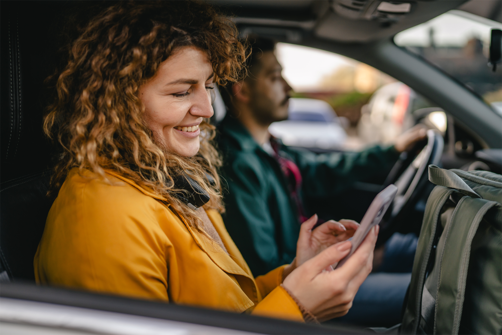 Smiling driver and passenger reviewing auto loan refinance options on a smartphone