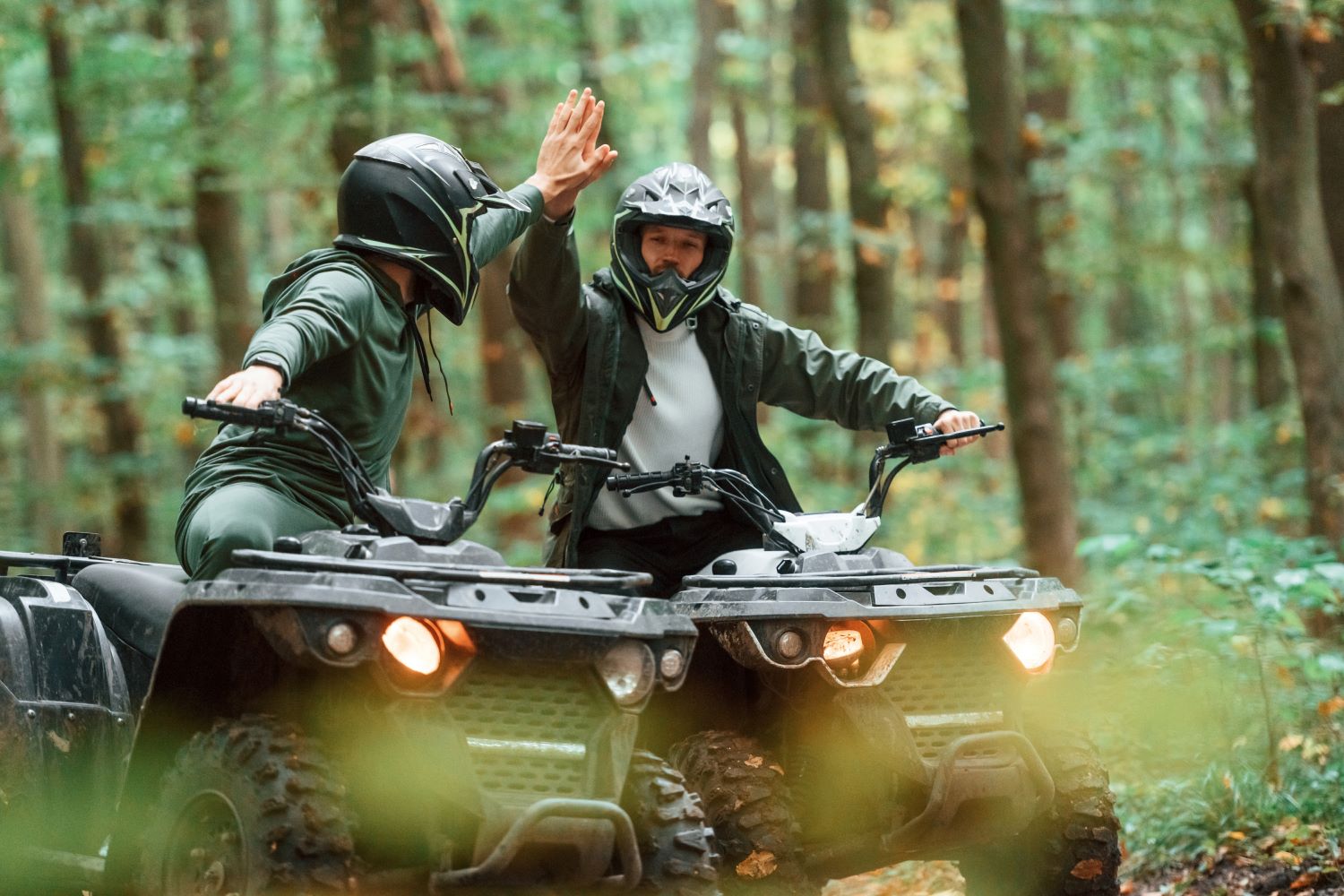 Two ATV riders exchange high fives in the forest